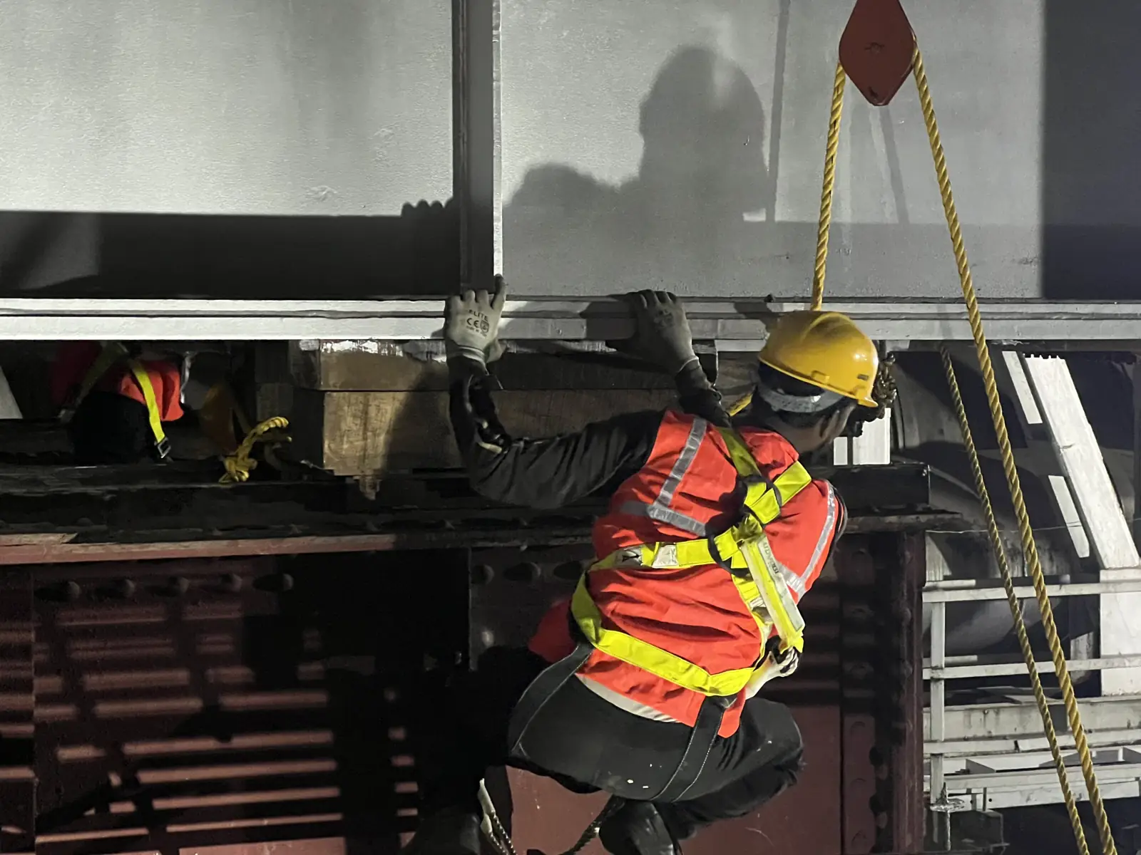 Erection crew in harnesses guiding a steel girder into place at night